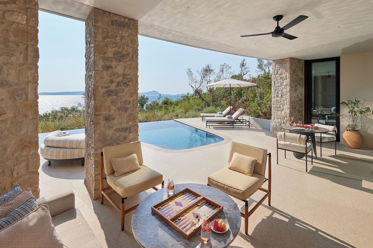 Un área junto a la piscina con sillones de descanso, una mesa de comedor y vista al mar.