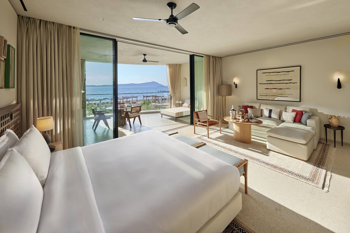 Una habitación de hotel amplia con una cama grande, un balcón con vistas al mar, un sofá y una mesita de café.