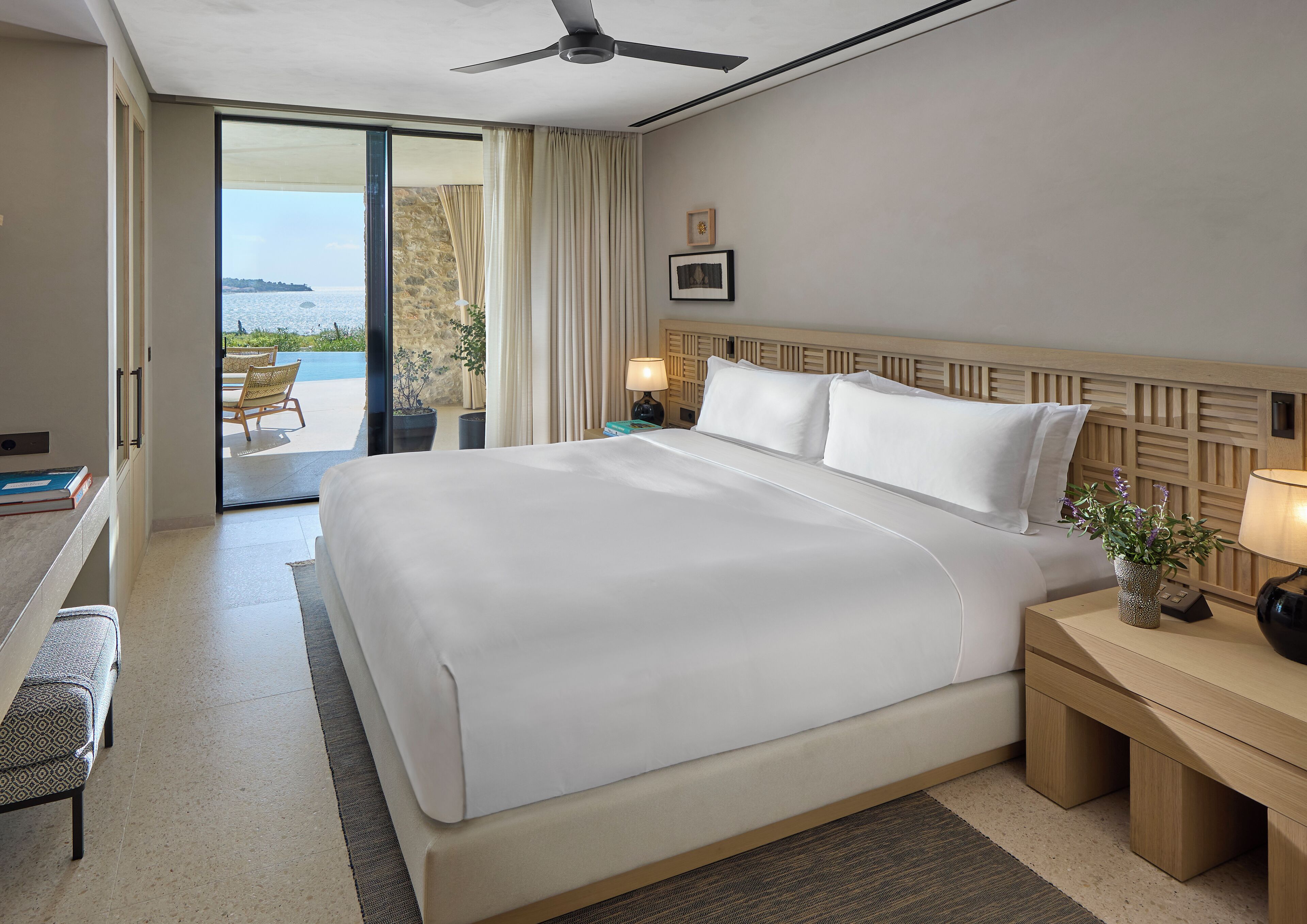 Une chambre d’hôtel avec un grand lit, un bureau, une chaise, une table de chevet, une lampe et une vue sur l’océan.