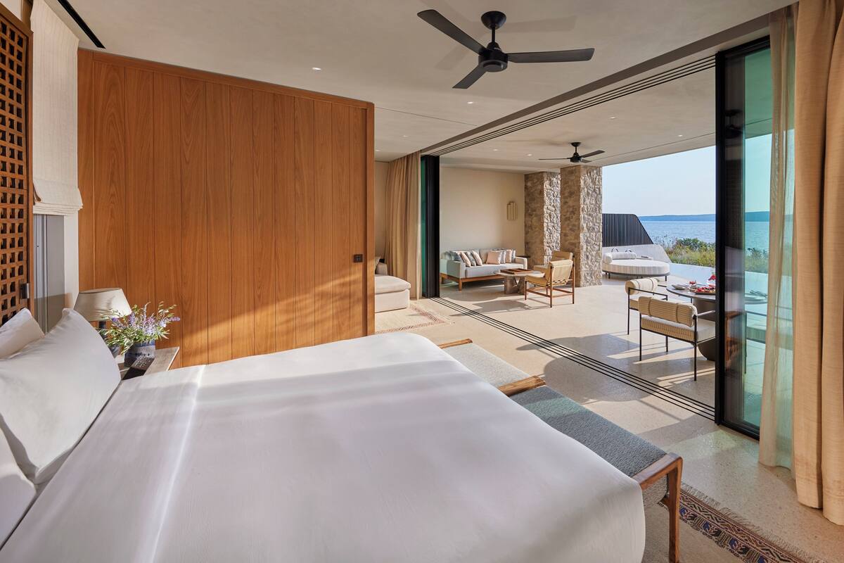 Habitación de hotel moderna con una cama grande, ventilador de techo y balcón con vistas al mar.