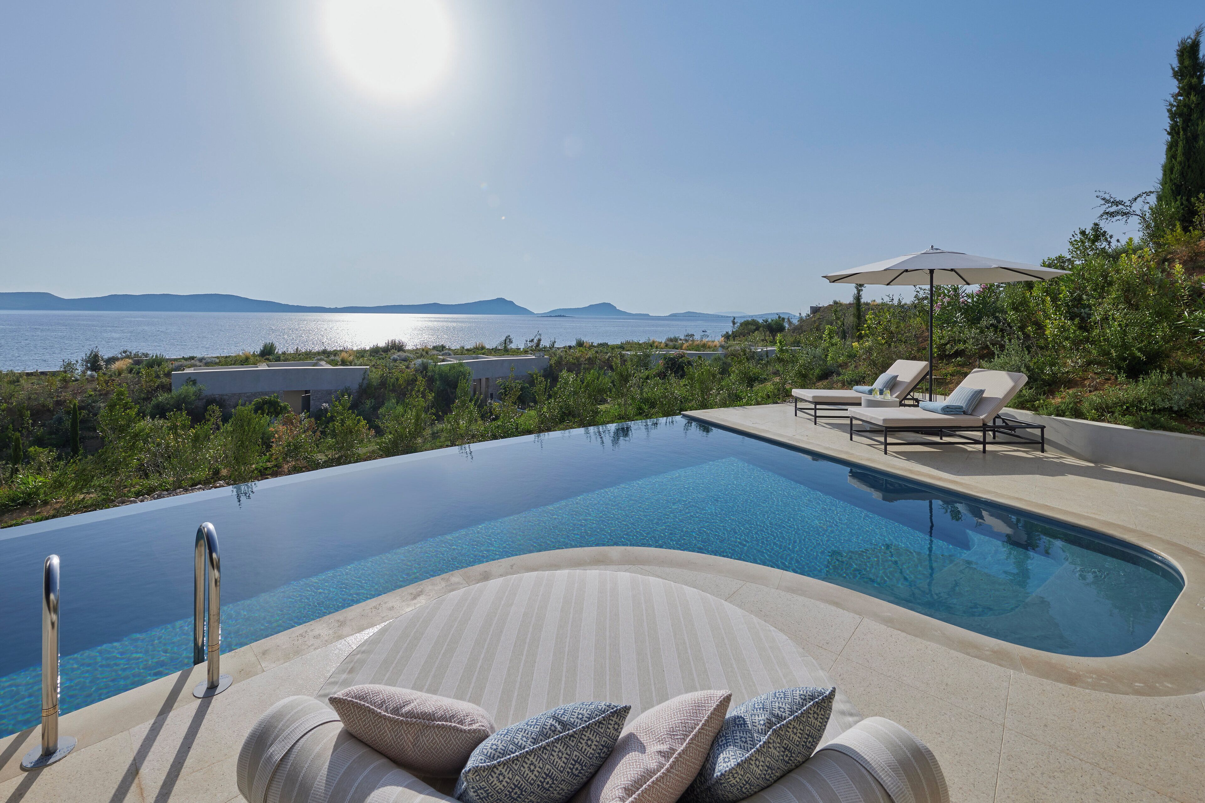 Una piscina con vistas al mar y a las montañas, sillas de descanso y una sombrilla.