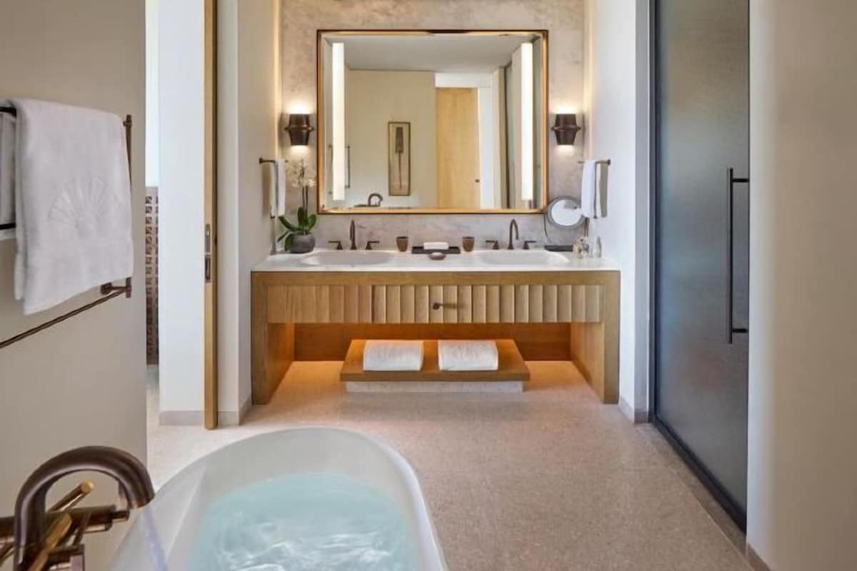A modern bathroom with a bathtub, two sinks, and a large mirror.