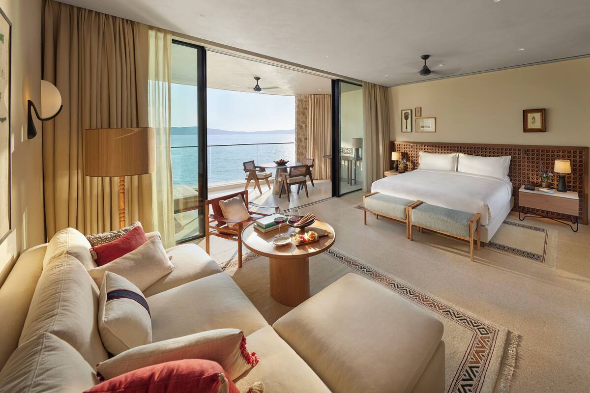 Habitación de hotel con una cama grande, un sofá, una mesa de comedor y un balcón con vistas al mar.