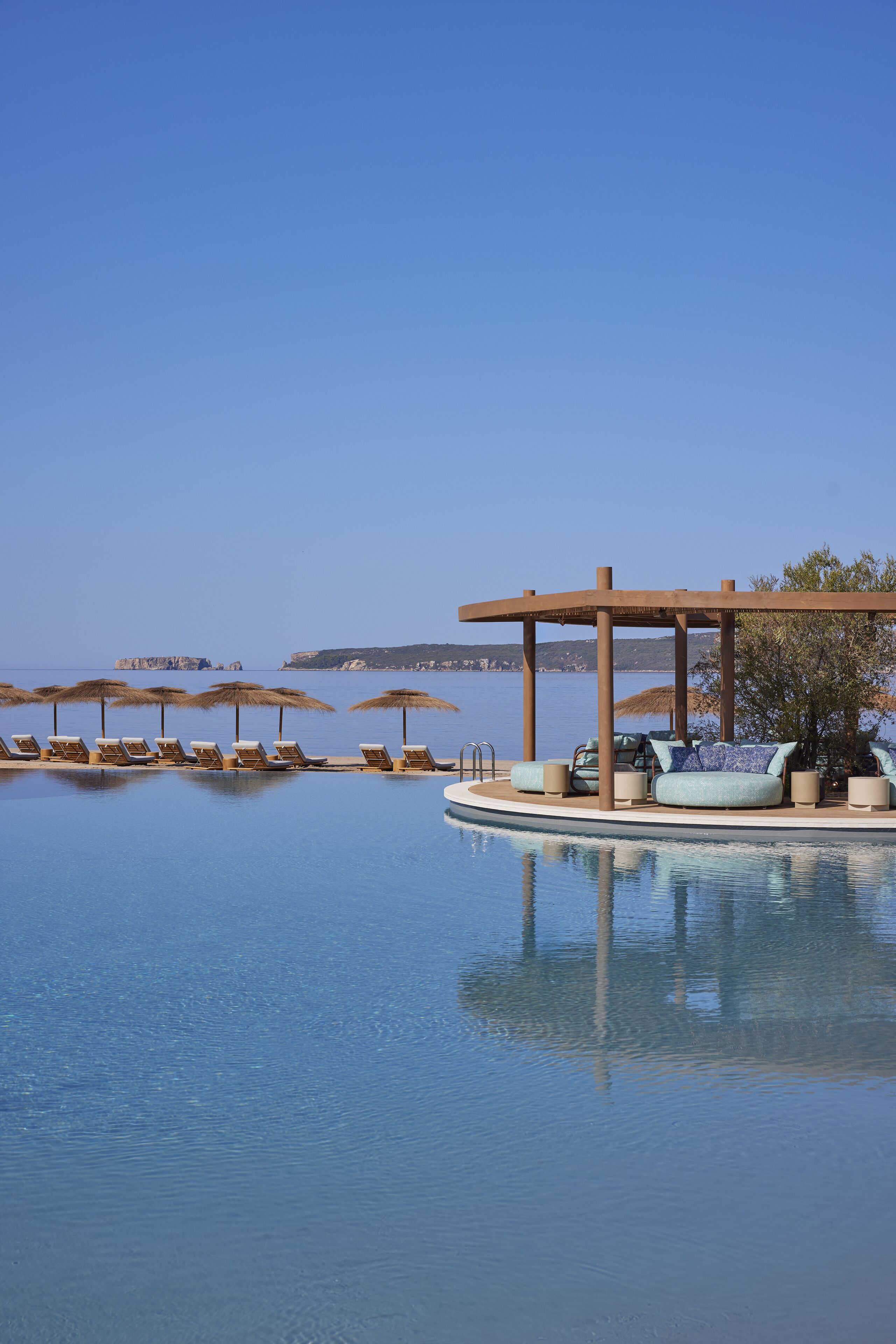 Área da piscina com espreguiçadeiras e guarda-sóis, um espaço de estar coberto e vista para o mar.