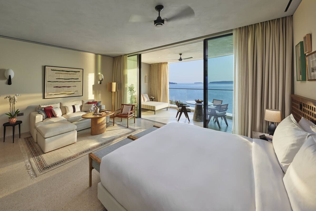 Una habitació d'hotel àmplia amb un llit gran, un sofà, una taula de menjador i un balcó amb vista al mar.