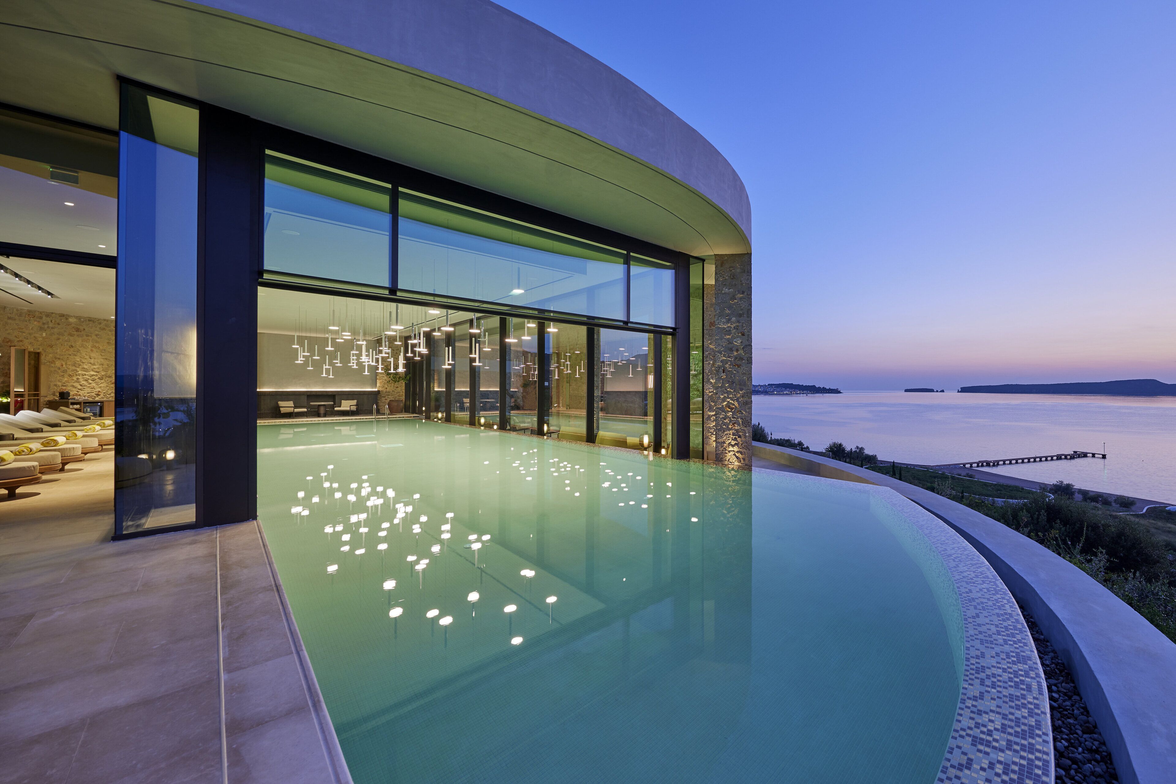 A modern building with a large pool, glass walls, and a view of the water.