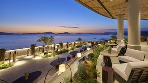 Un espacio al aire libre con mesas y sillas, plantas en macetas y vistas al mar y a las montañas.