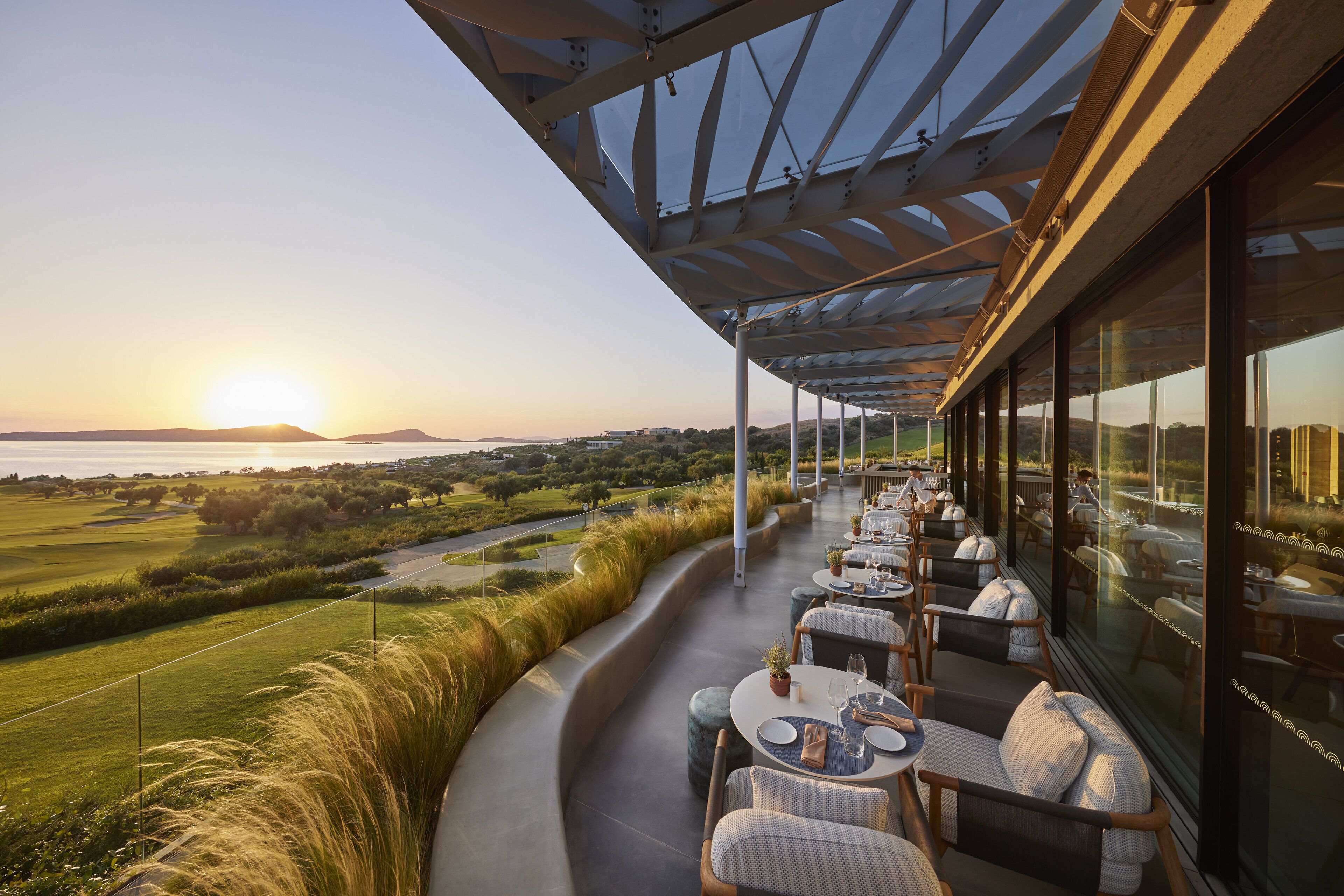 A restaurant with outdoor seating overlooking a scenic landscape, including a golf course and a body of water.