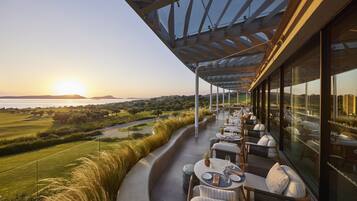 A restaurant with outdoor seating overlooking a scenic landscape, including a golf course and a body of water.