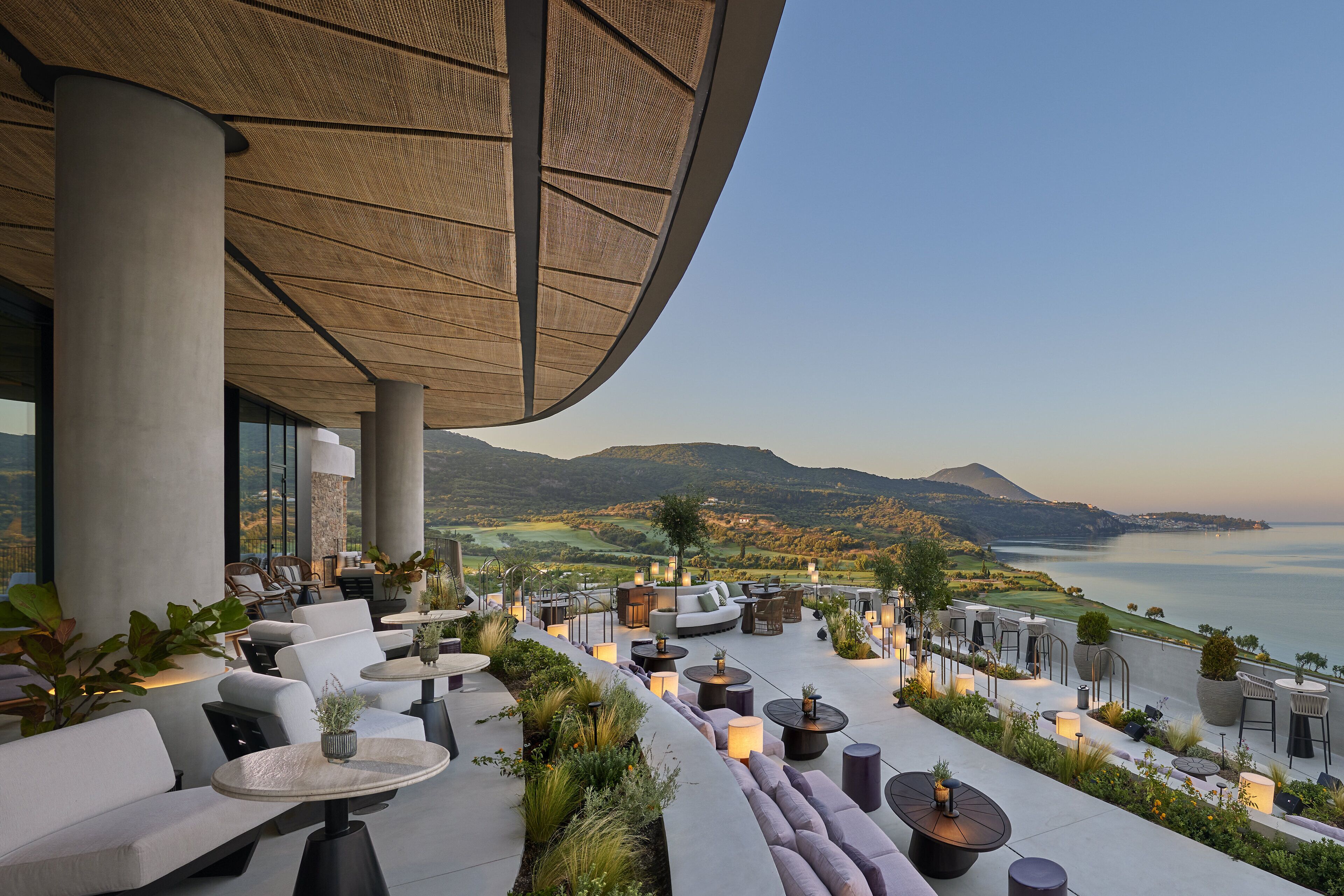 Een terras met moderne meubels, uitzicht op zee en bergen op de achtergrond.