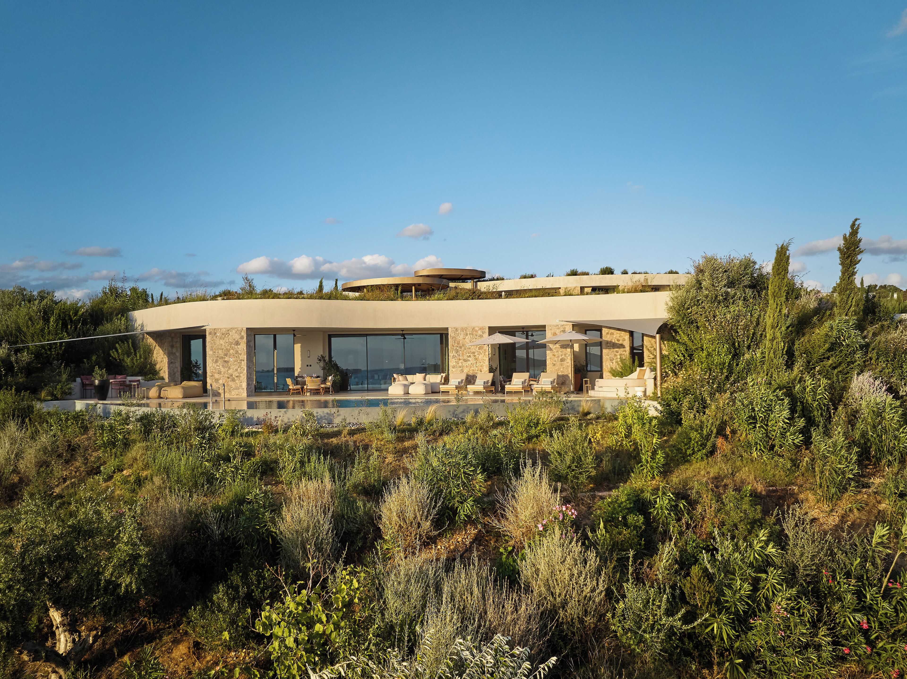 Ein modernes Haus mit Pool, Sitzgelegenheit im Freien und Blick auf die umliegende Vegetation.