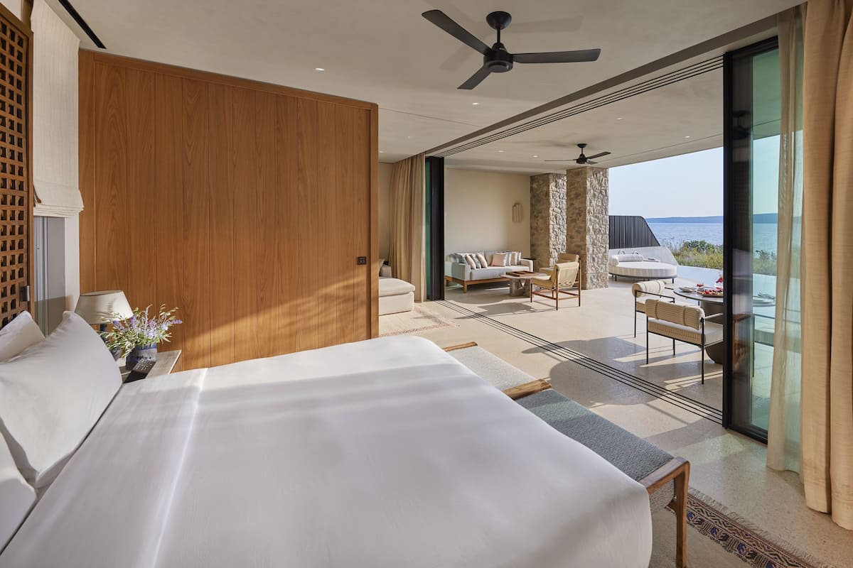 Habitación de hotel moderna con una cama grande, ventilador de techo y balcón con vistas al mar.