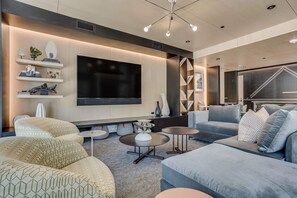 A modern living room with a large flat-screen TV, comfortable seating, and decorative shelves.
