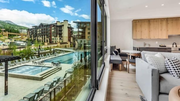 Ein modernes Wohnzimmer mit großem Fenster, das einen Blick auf einen Pool und andere Gebäude bietet.
