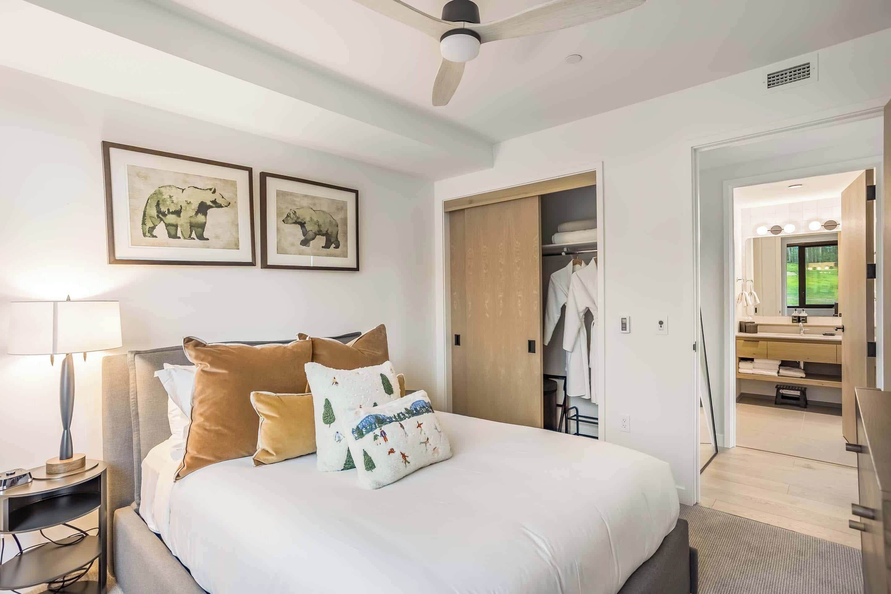 A modern hotel room with a large bed, a bedside table with a lamp, and a wardrobe.