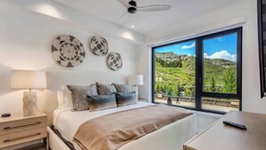 Ein modernes Schlafzimmer mit einem großen Bett, Nachttischen und Blick auf eine Berglandschaft durch große Fenster.