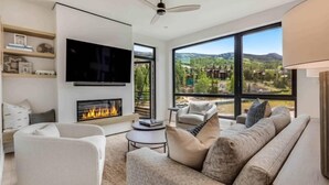 A modern living room with a fireplace, a flat-screen TV, and a large window offering a mountain view. - Electric Pass Lodge 509 (Snowmass Village)
