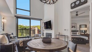 A modern living room with a round wooden table, a sofa, and a TV mounted on the wall. - Electric Pass Lodge 607 (Snowmass Village)
