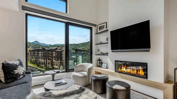 A modern living room with a large window, a fireplace, a flat-screen TV, and a sofa. - Electric Pass Lodge 607 (Snowmass Village)