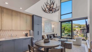 A modern kitchen with a dining area, large windows with a view of a town, and a chandelier. - Electric Pass Lodge 607 (Snowmass Village)