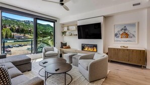 A modern living room with a fireplace, comfortable seating, a flat-screen TV, and a large window offering a scenic view.