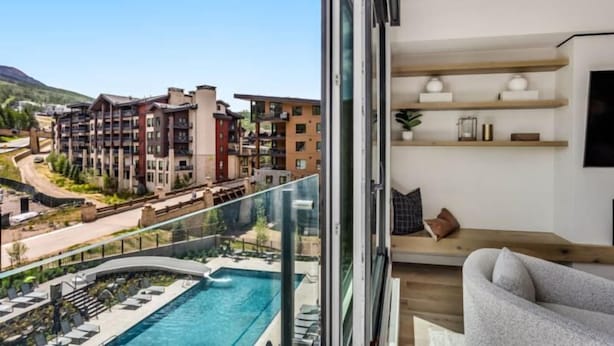 A modern hotel room with a large balcony, a pool, and a view of other hotel buildings.