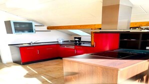A modern kitchen with red cabinets, a central island, and a built-in stove. - Jünkerath Romantic Garden Stay (Jünkerath)