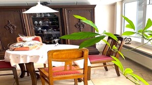 A dining area with a round table, chairs, a cabinet, and a window with a plant. - Jünkerath Romantic Garden Stay (Jünkerath)