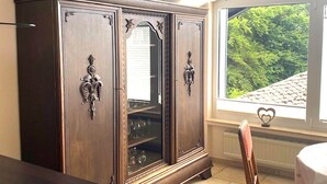 A dark wooden cabinet with ornate handles and glass doors, positioned near a window with a view of greenery. - Jünkerath Romantic Garden Stay (Jünkerath)