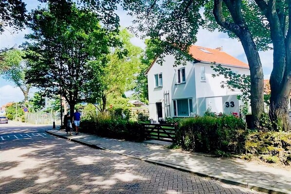 A residential street with a white house numbered 33, a paved sidewalk, and trees.