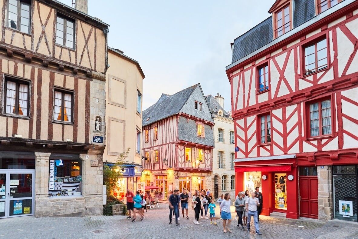 Une rue pavée bordée de bâtiments traditionnels à colombages, avec un café et une librairie.
