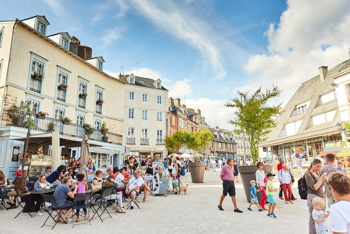 Een levendig caféterras met tafels en stoelen, omgeven door historische gebouwen met balkons en ramen.