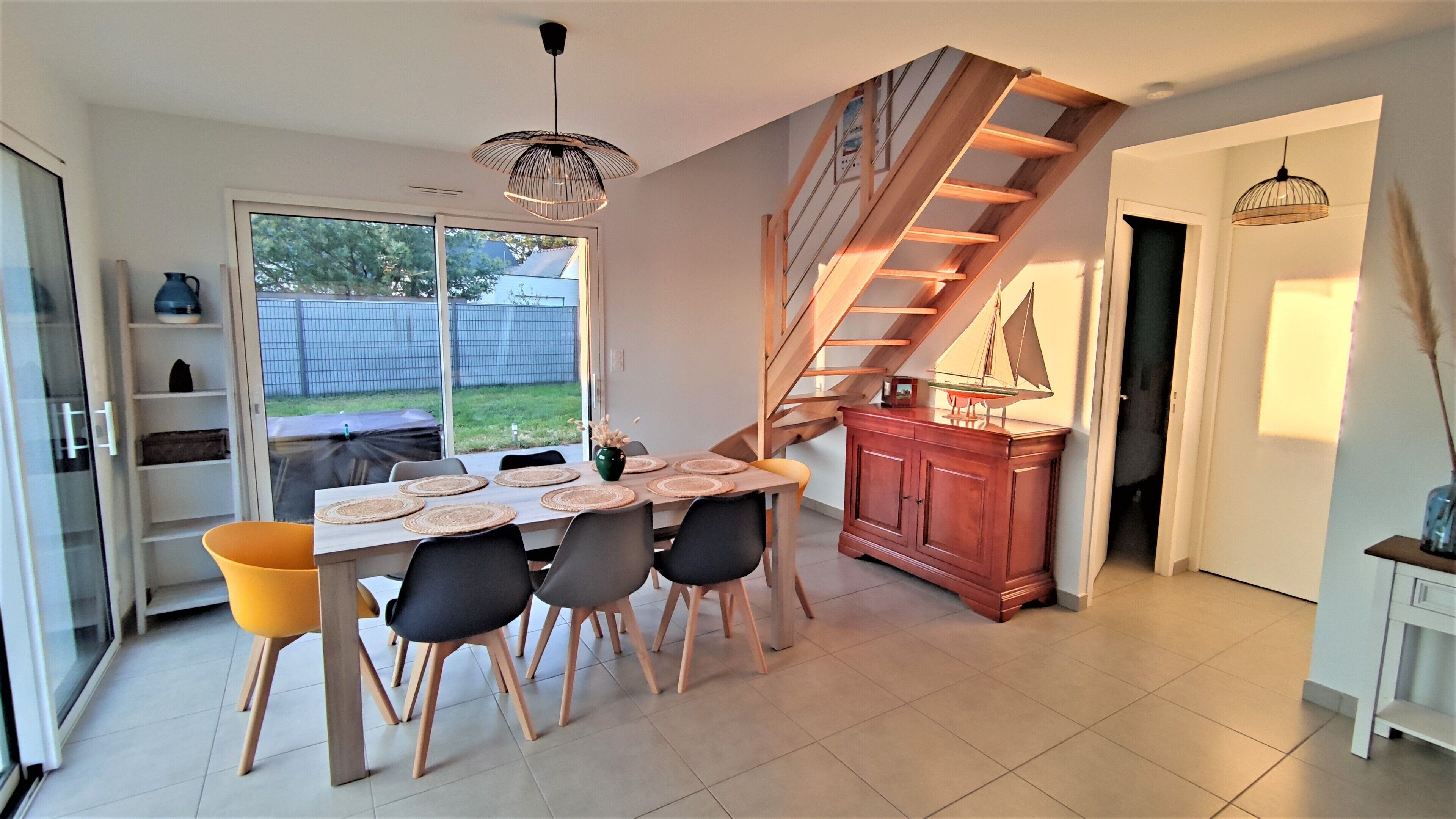 Un comedor con una mesa y sillas de madera, una escalera y vistas al exterior.