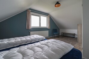 A dormitory room with two beds, a window with curtains, a radiator, a chair, and a bench. - Beautiful holiday home with hot tub (Makkum)