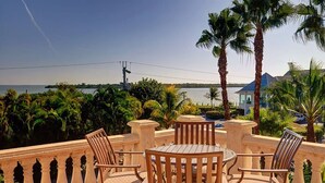 A terrace with a round table and four chairs, overlooking a body of water and palm trees. - Sandcastle Captiva luxurious, 2 minutes from beach, private pool, bay views (Captiva)