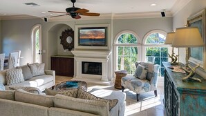 A spacious living room with a fireplace, comfortable seating, and large windows offering a view of the outdoors. - Sandcastle Captiva luxurious, 2 minutes from beach, private pool, bay views (Captiva)