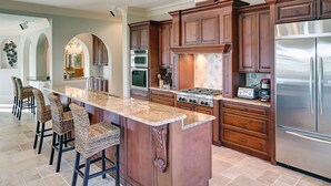 A kitchen with a large island, dark wooden cabinets, stainless steel appliances, and a bar area with wicker chairs. - Sandcastle Captiva luxurious, 2 minutes from beach, private pool, bay views (Captiva)