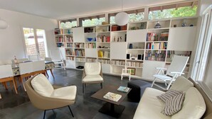 A modern living room with a large bookshelf, comfortable seating, and a dining area. - Perfect vacation house in the 44ha of Cap Ferret (Lège-Cap-Ferret)