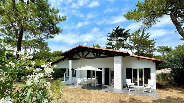 A modern house with a covered patio, outdoor seating, and a garden with white flowers. - Perfect vacation house in the 44ha of Cap Ferret (Lège-Cap-Ferret)