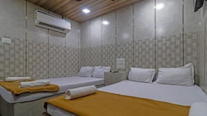 A hotel room with two beds, each with white linens and a mustard-colored blanket. There is an air conditioning unit mounted on the wall above the beds. - Capital Guest House (Mumbai)