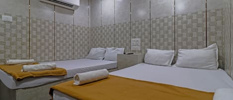 A hotel room with two beds, each with white linens and a mustard-colored blanket. There is an air conditioning unit mounted on the wall above the beds.