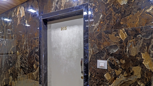 A marble elevator door with the number 215, a metallic handle, and a light switch on the wall. - Capital Guest House (Mumbai)