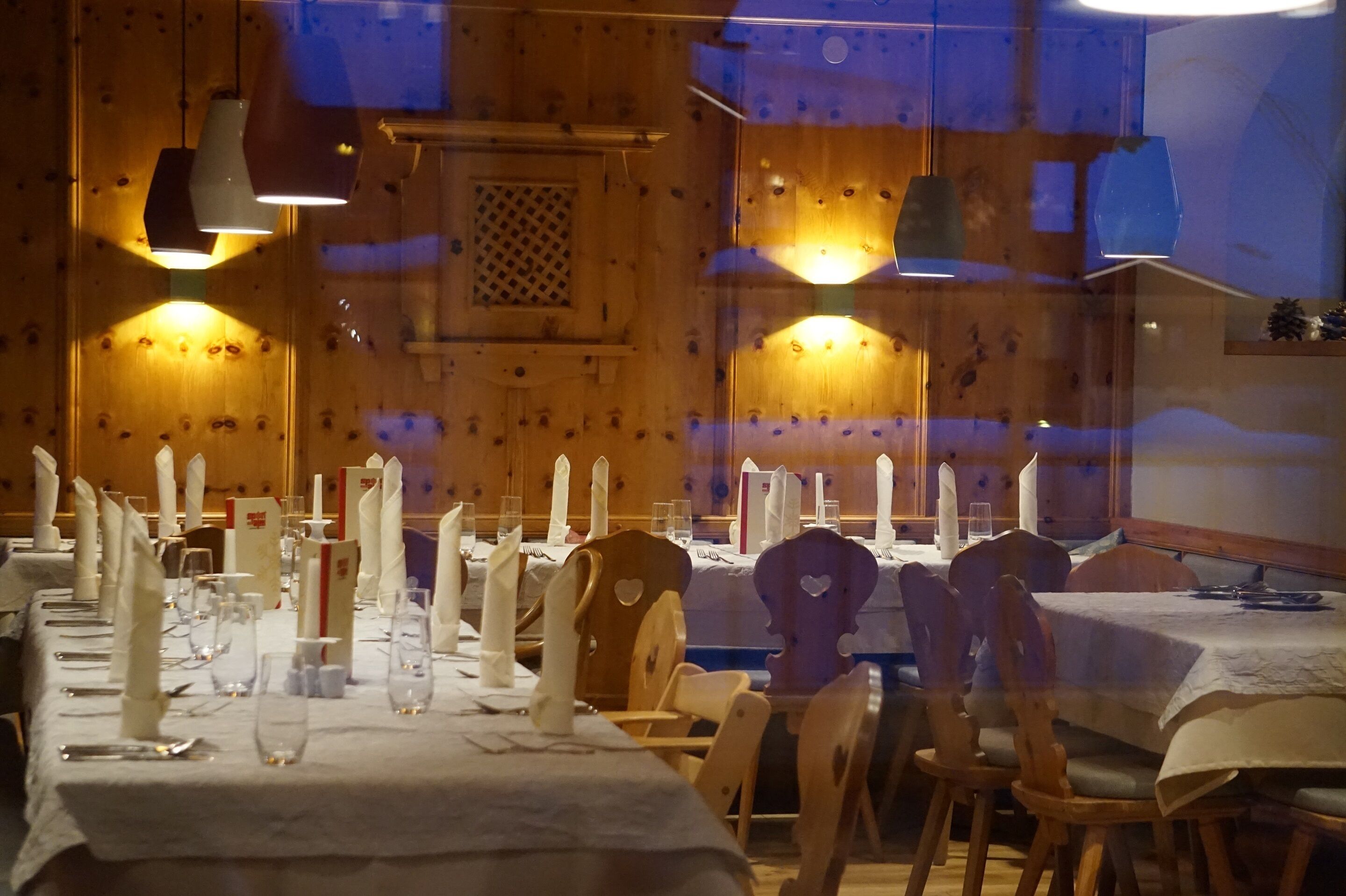 A dining area with wooden tables set for a meal, featuring white tablecloths, napkins, and candles.