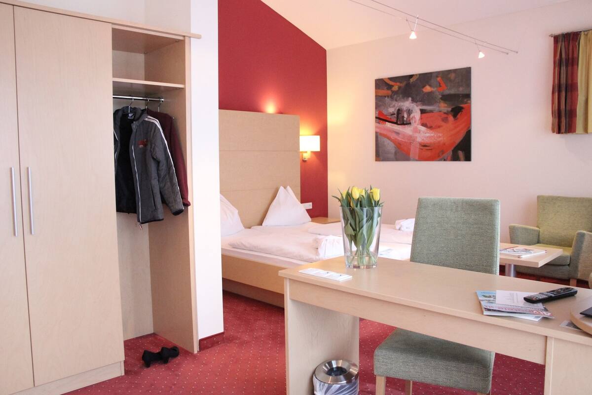 Une chambre d’hôtel avec un lit, un bureau et une chaise, une armoire et un tableau au mur.