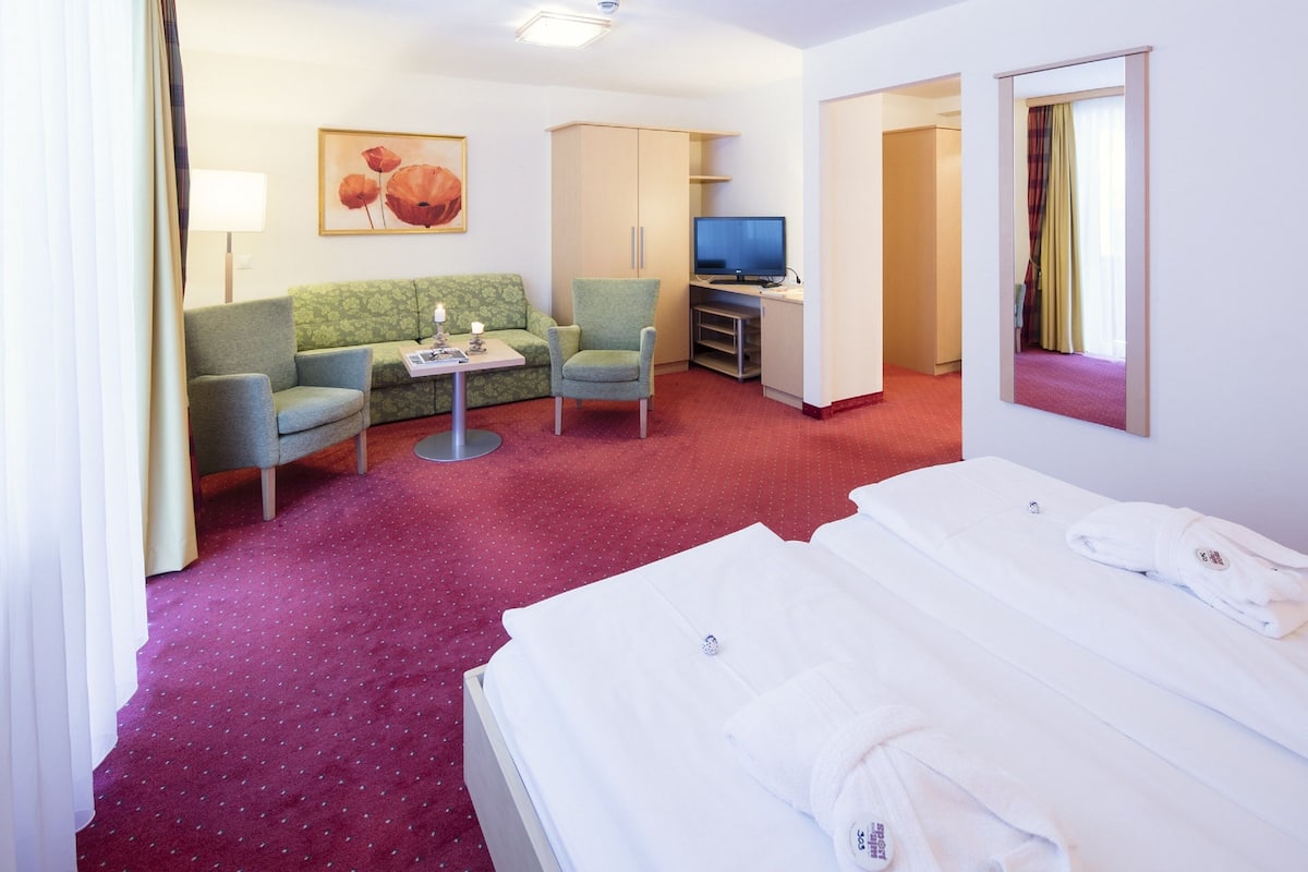 Une chambre d’hôtel avec un lit, un canapé vert, une petite table, une télévision et un miroir.
