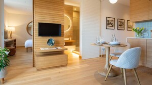 A modern hotel room with a wooden wall, a flat-screen TV, a dining area with a table and chairs, and a kitchen area with a sink and cabinets. - NEW, REFINED, ELEGANT AND EXCLUSIVE APARTMENT LOCATED IN THE CENTER OF THE CITY. (Agrigento)