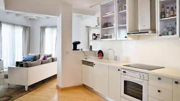 Una cocina moderna con armarios blancos, horno integrado y un comedor con sofá y cortinas.
