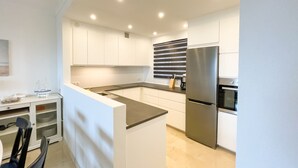 Una cocina moderna con armarios blancos, un refrigerador de acero inoxidable y una encimera negra.