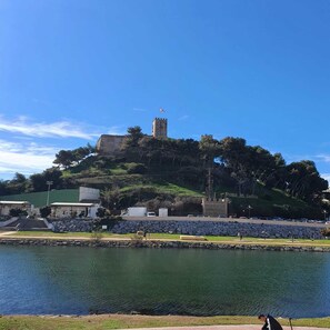 Un château perché sur une colline, dominant une étendue d’eau, avec un mur de pierre et une pancarte indiquant « Parque del Castillo ».