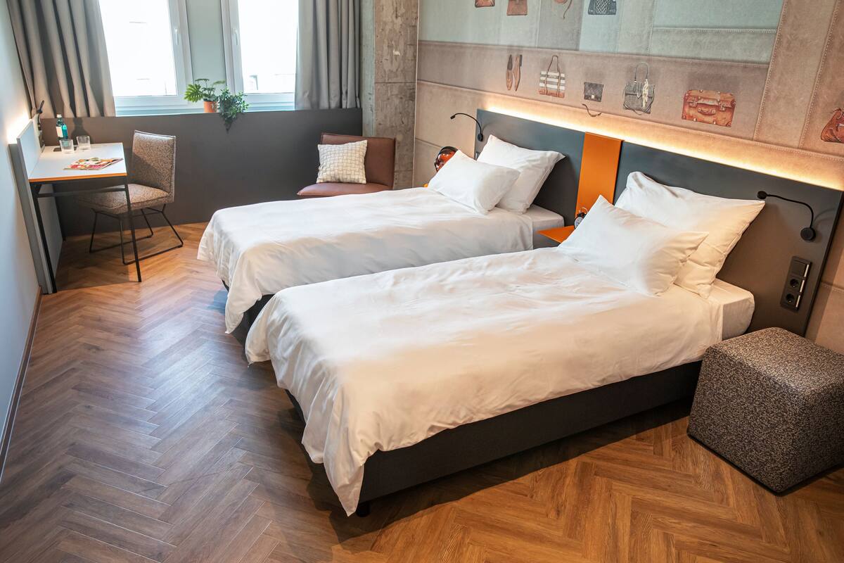 A hotel room with two beds, a desk, and a potted plant by the window.